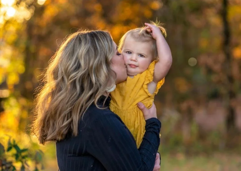 mother holding her baby surrounded by fall trees